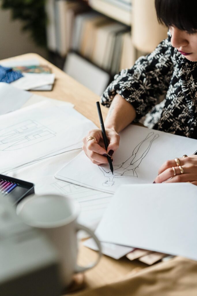 Talented crop woman drawing clothing design at table on blurred background in daylight
